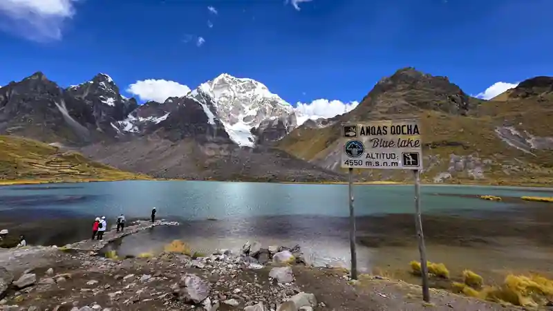 Letrero informativo de la laguna Anqas Qocha frente a las aguas cristalinas en Cusco.