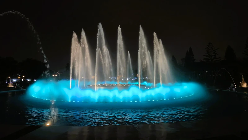 Chorros de agua gigantes iluminados con color turquesa brillante en la fuente de la fantasia del Parque de la Reserva.