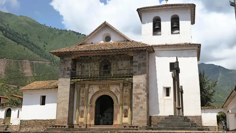 Vista exterior de la famosa iglesia de Andahuaylillas con su campanario y cruces de piedra bajo el cielo andino.